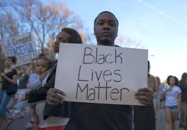 Man holds "Black Lives Matter" sign at protest. "Black Lives Matter" by Fibonacci Blue is licensed with CC BY 2.0. To view a copy of this license, visit https://creativecommons.org/licenses/by/2.0/
