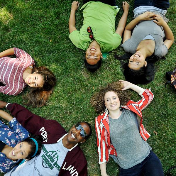 Students lying in grass looking up at camera