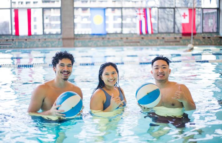 Three people standing in the Rec Center pool posing with beach balls.