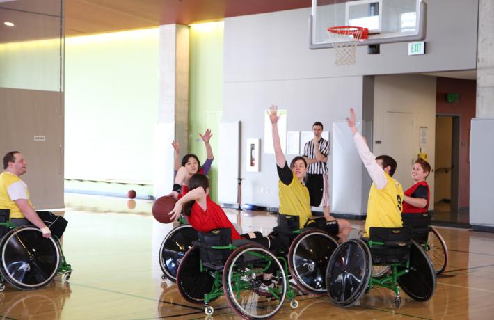 A game of wheelchair basketball and the yellow team guards the red team from shooting. 