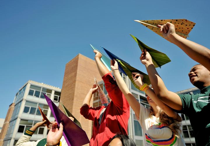 Students holding paper airplanes to the sky.